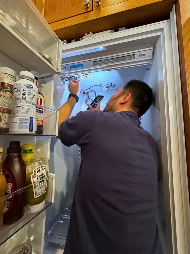 Technician checking the control board at the top of a panel-ready built-in refrigerator